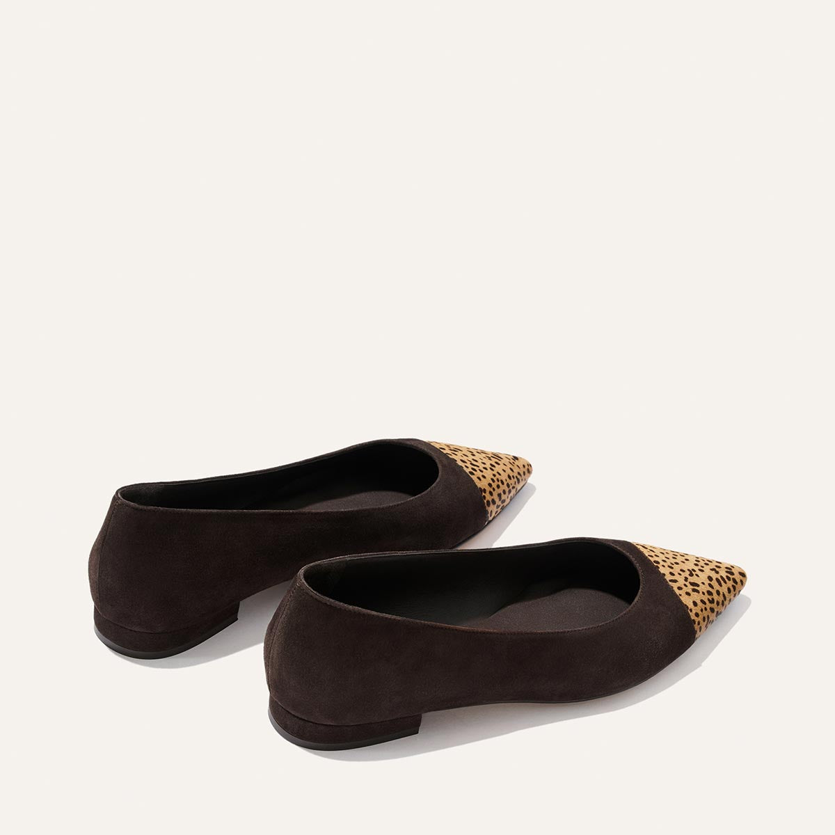 A pair of The Alba - Molasses Suede and Tan Mini Cheetah Haircalf ballet flats by Margaux, featuring black suede with tan and black mini cheetah print accents on the pointed toe, displayed on a plain, light background.