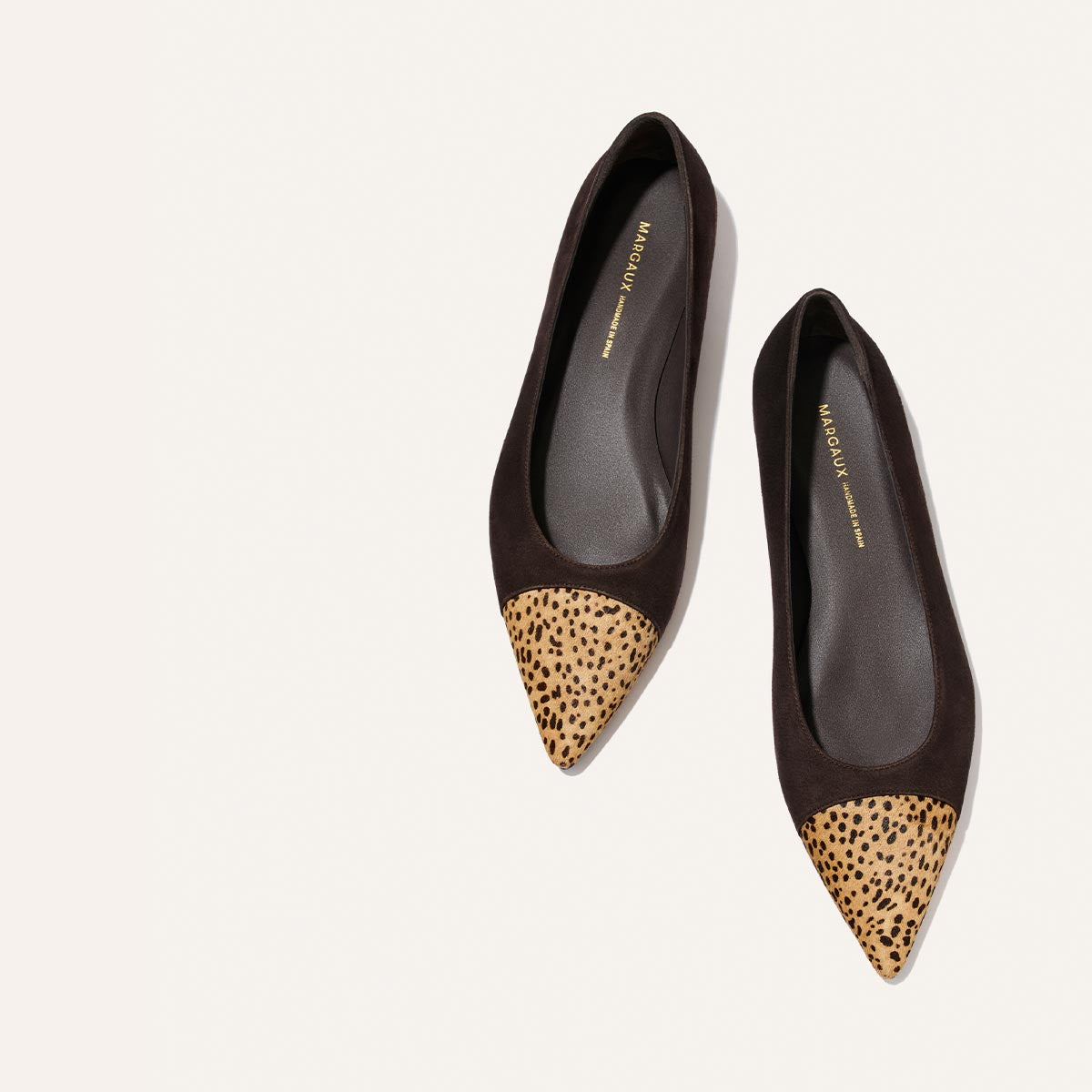 A pair of Margaux’s “The Alba” flats in molasses suede, featuring a chic pointed toe with tan mini cheetah haircalf detailing, displayed on a light background.