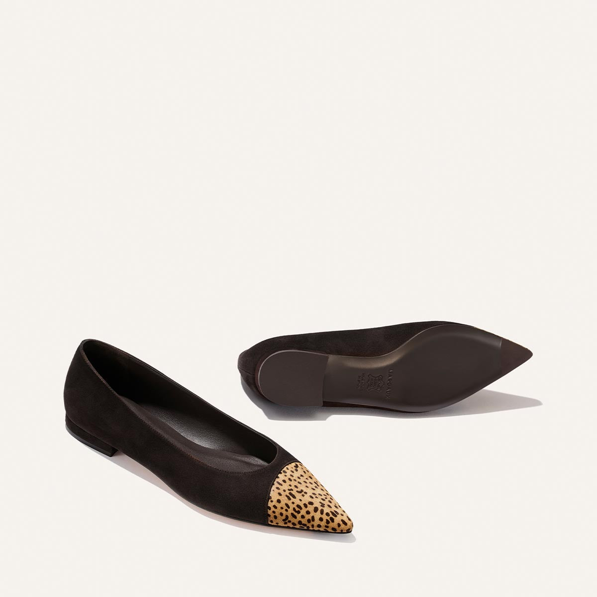 A pair of Margaux “The Alba” flats in molasses suede, featuring a pointed toe and tan mini cheetah haircalf detail at the front, displayed from the side and bottom views against a plain background.