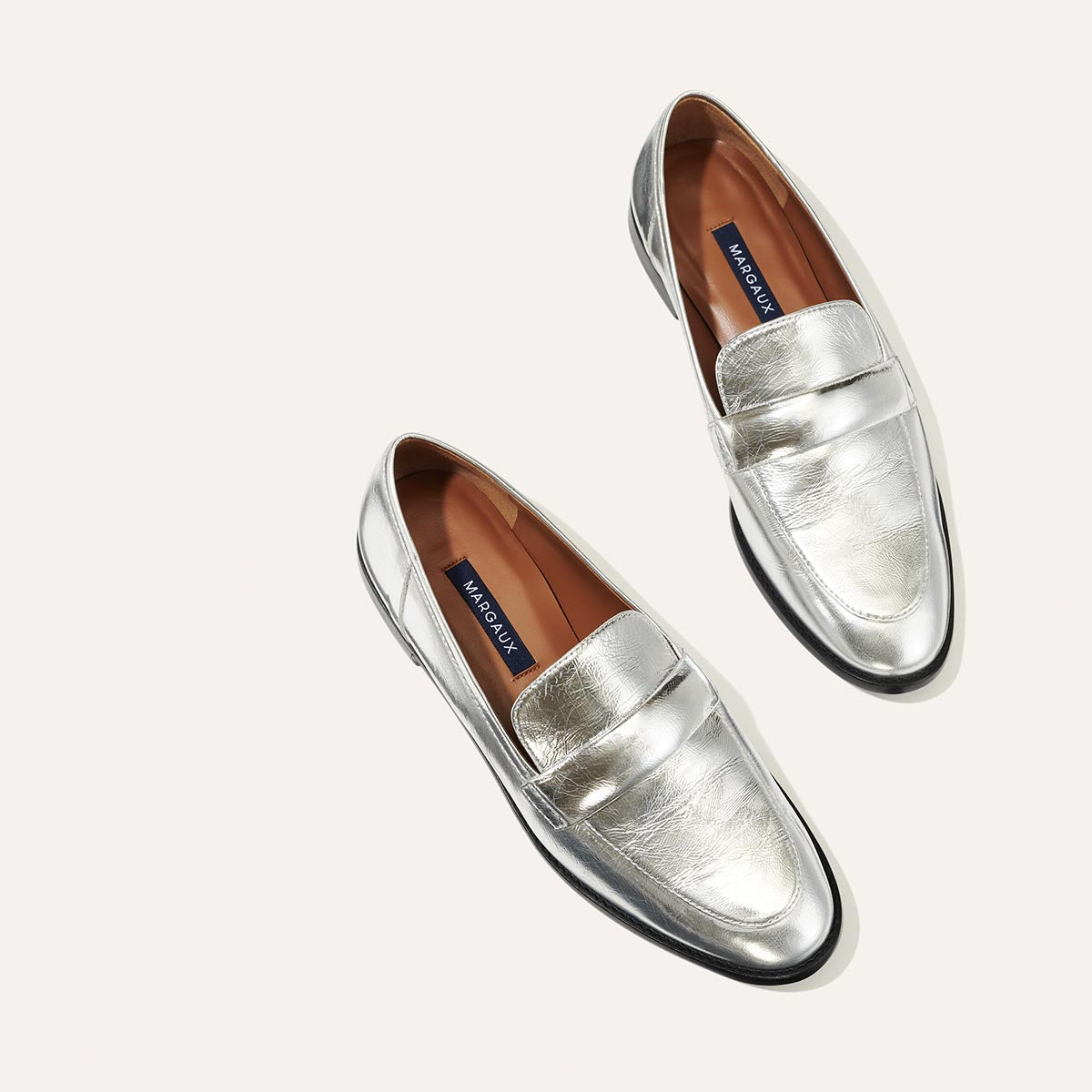 The Andie Loafer in shiny Silver Crinkle Mirror, featuring a sleek structured design made from smooth Italian nappa leather with a minimalistic padded keeper detail.