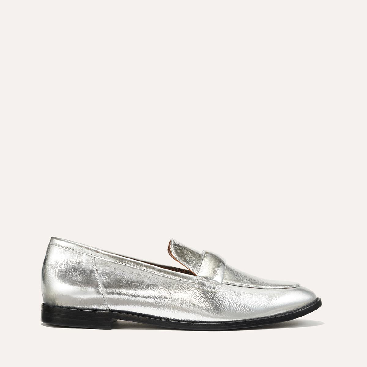 The Andie Loafer in shiny Silver Crinkle Mirror, featuring a sleek structured design made from smooth Italian nappa leather with a minimalistic padded keeper detail.