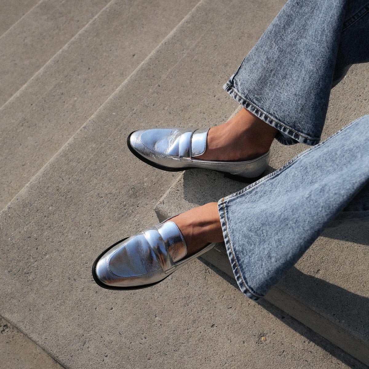 The Andie Loafer in shiny Silver Crinkle Mirror, featuring a sleek structured design made from smooth Italian nappa leather with a minimalistic padded keeper detail.