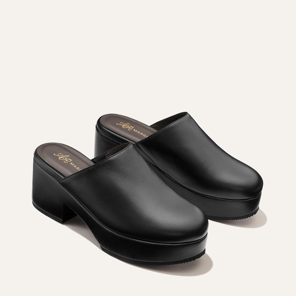 A pair of The Atlantic Clog in Black Calf by Margaux, featuring black leather with closed toes and chunky platform heels, set against a plain off-white background.