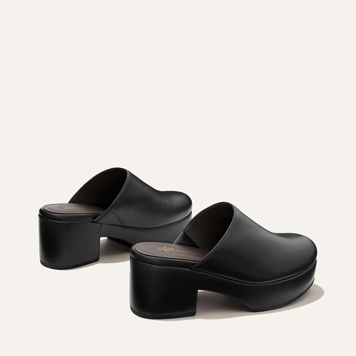 A pair of Alison Roman x Margaux: The Atlantic Clog in Black Calf by Margaux, featuring black leather platform soles and chunky heels, displayed on a plain, light background.