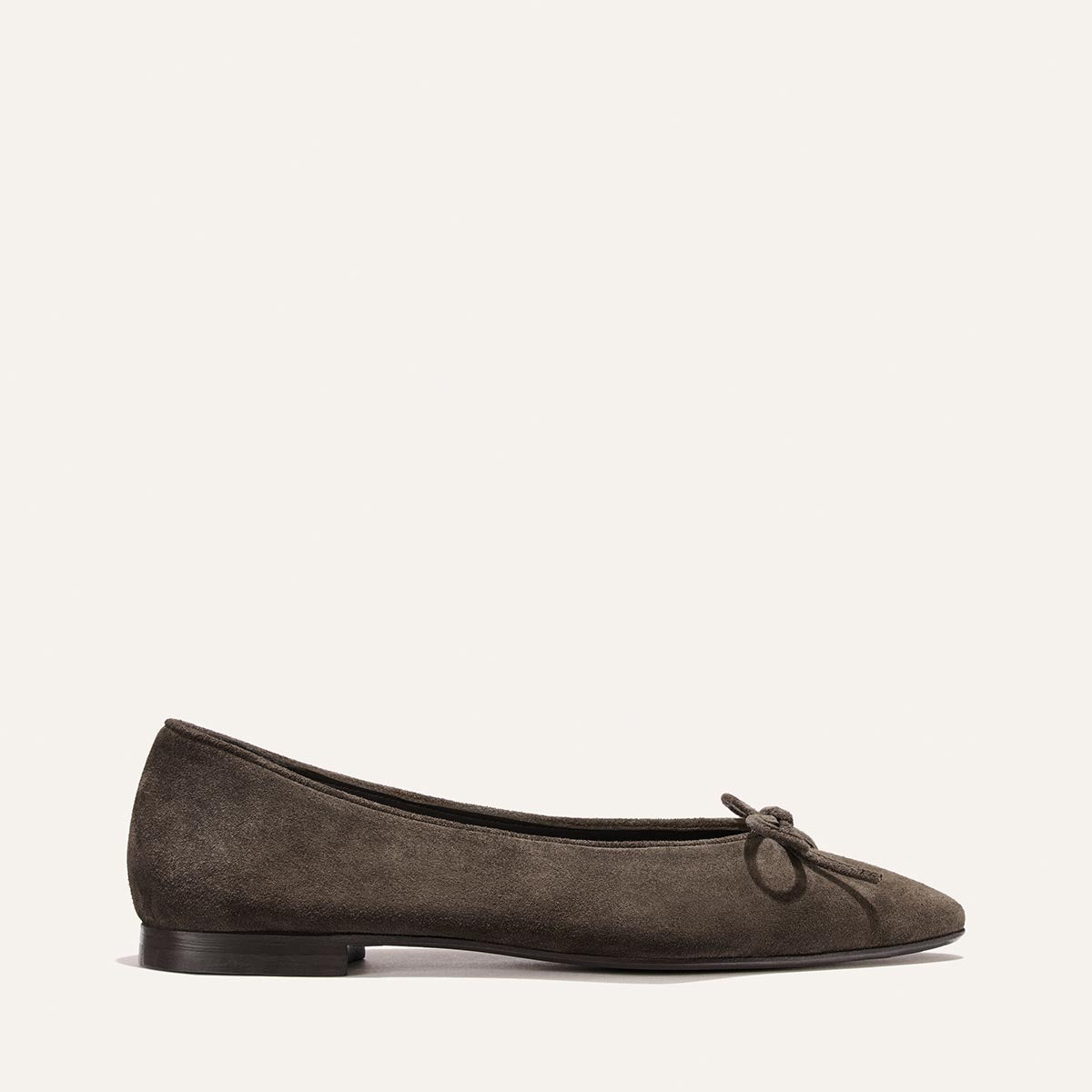 The Alison Roman x Margaux: The Salamanca - English Brown Suede by Margaux is a single dark brown suede ballet flat with a small bow on the toe, featuring an unlined construction for exceptional comfort, displayed on a plain light background.
