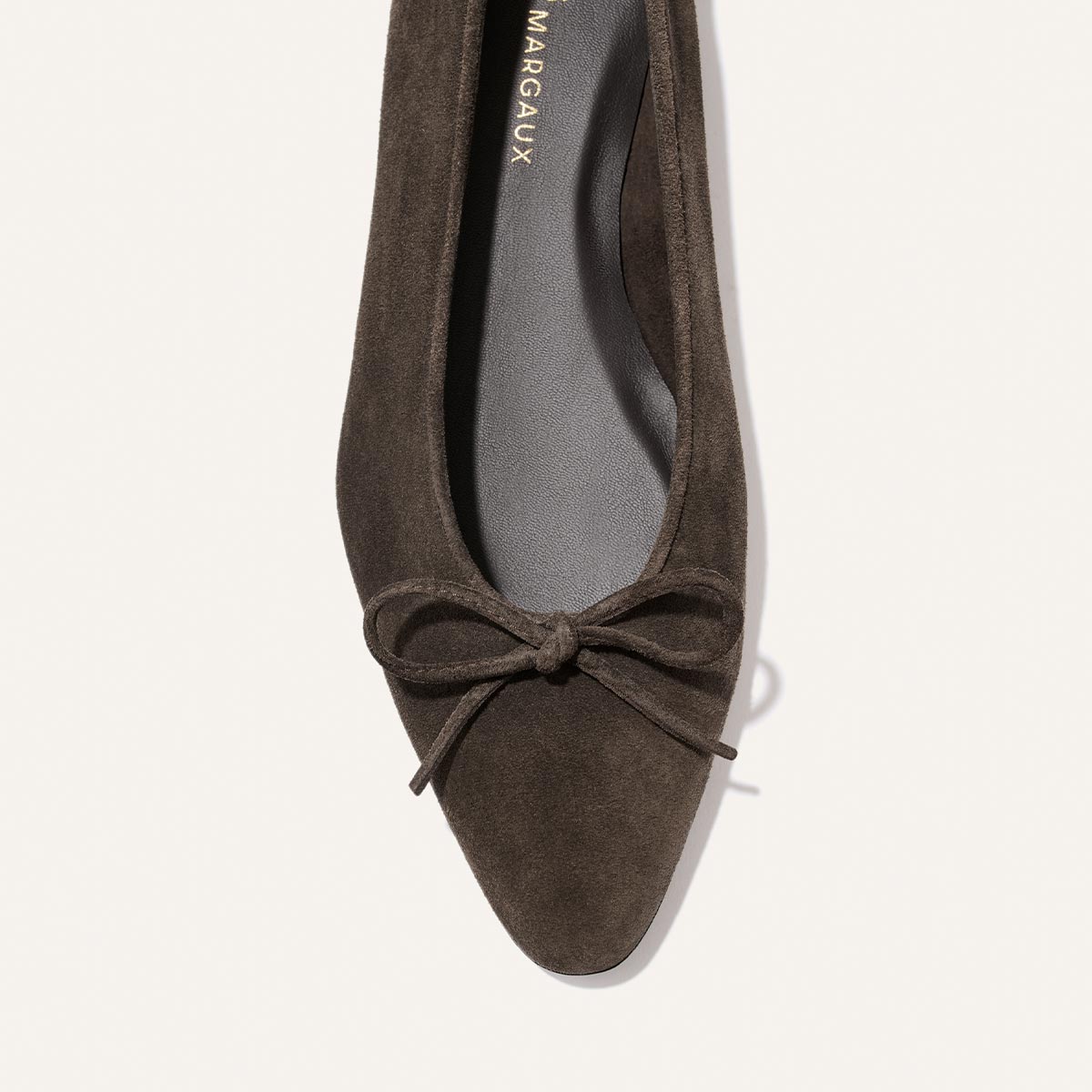 A top view of the Margaux Alison Roman x Margaux: The Salamanca flat in English Brown Suede, showcasing buttery soft leather with a pointed toe, front bow detail, unlined construction, and a black insole.