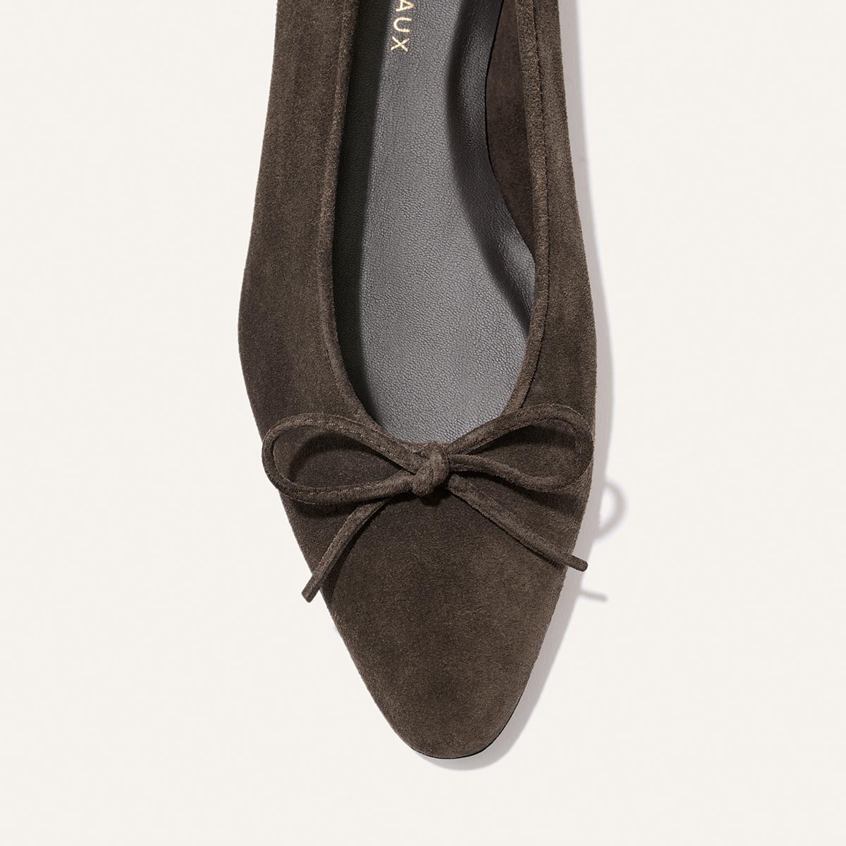 A close-up of the Alison Roman x Margaux: The Salamanca - English Brown Suede, a pointed-toe ballet flat with a front bow, shown from above against a light background.
