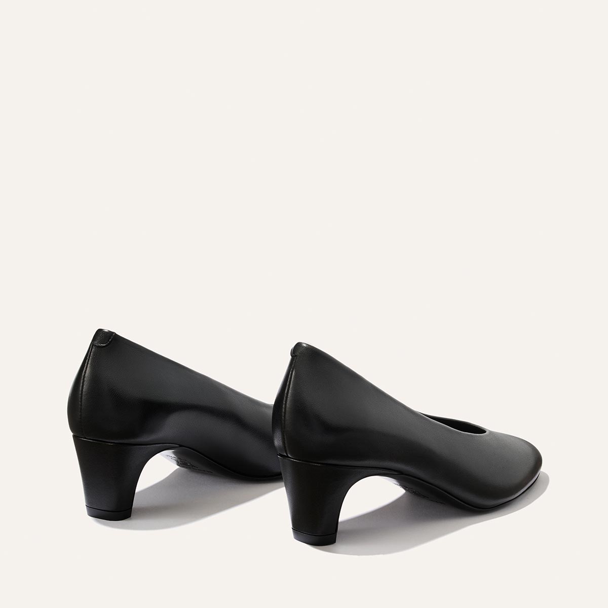 A pair of Margaux’s The Augusta Glove Pump in Black Nappa is displayed on a light background, with one shoe facing forward and the other turned slightly to the side.