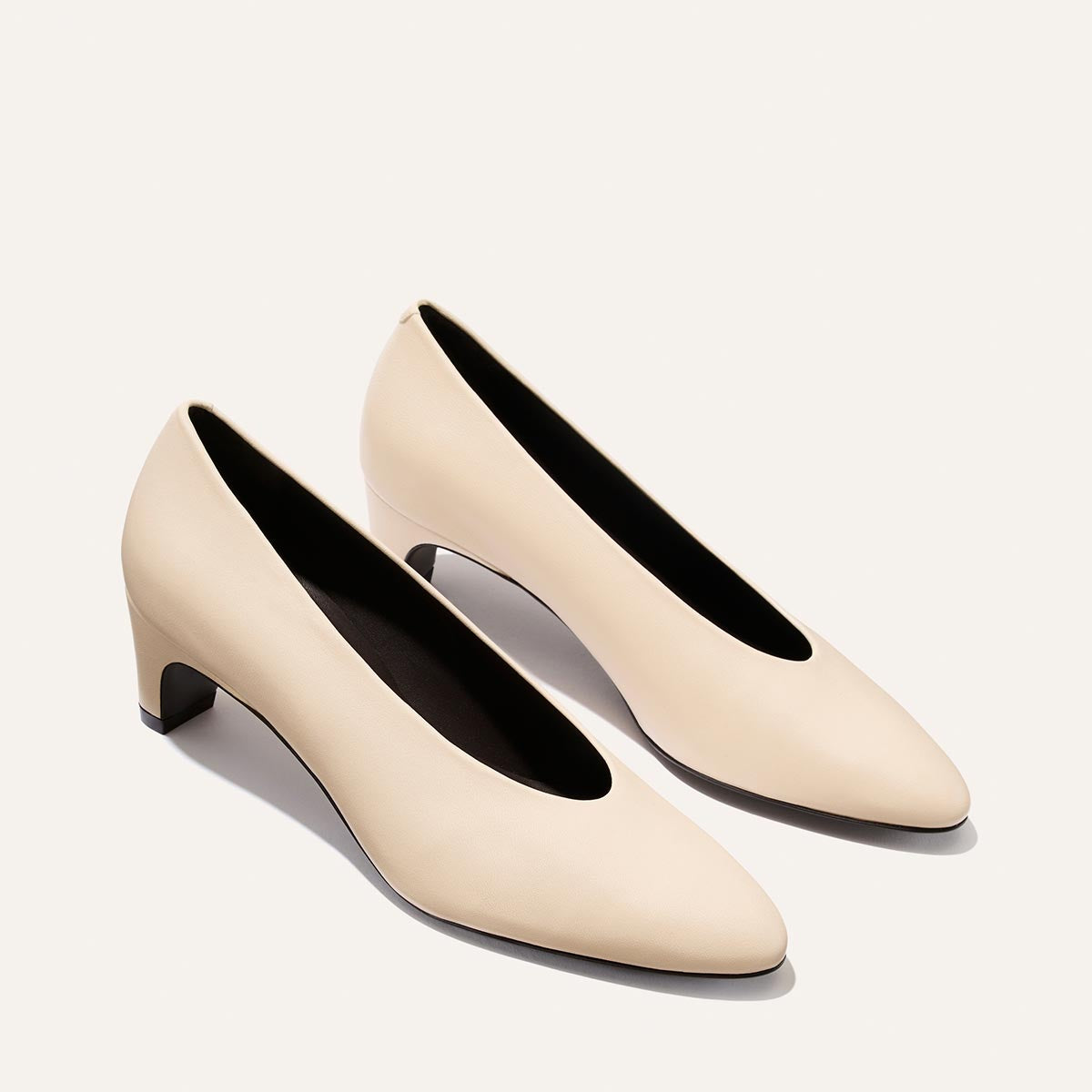 A pair of Margaux’s The Augusta Glove Pump in Bone Nappa—a beige, closed-toe, low-heeled women’s pump—is displayed on a plain light background, angled slightly to the side.