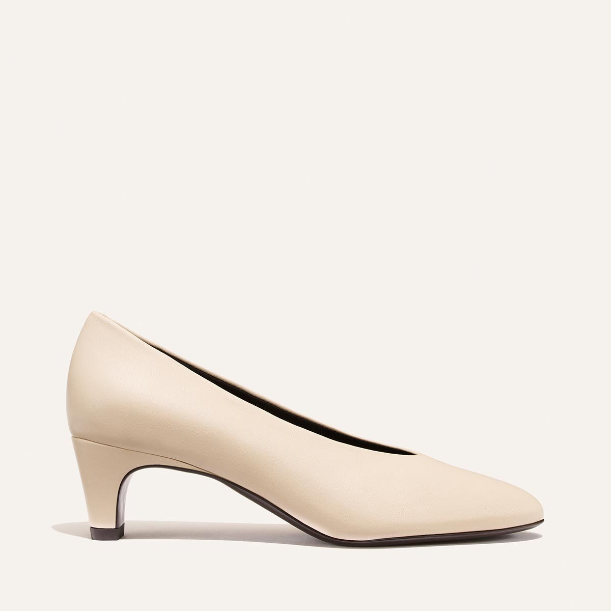 The Augusta Glove Pump by Margaux in Bone Nappa is displayed in profile against a plain, light background. This women’s dress shoe features a rounded toe and a short, slightly tapered heel.