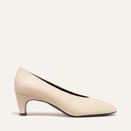 The Augusta Glove Pump by Margaux in Bone Nappa is displayed in profile against a plain, light background. This women’s dress shoe features a rounded toe and a short, slightly tapered heel.