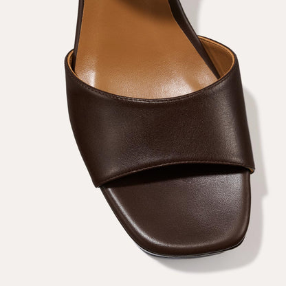 Close-up of The Bardi - Espresso Calf by margaux-development: a dark brown, open-toe sandal with a wide leather strap, square toe, tan footbed, and platform heel, shown from above against a light backdrop.