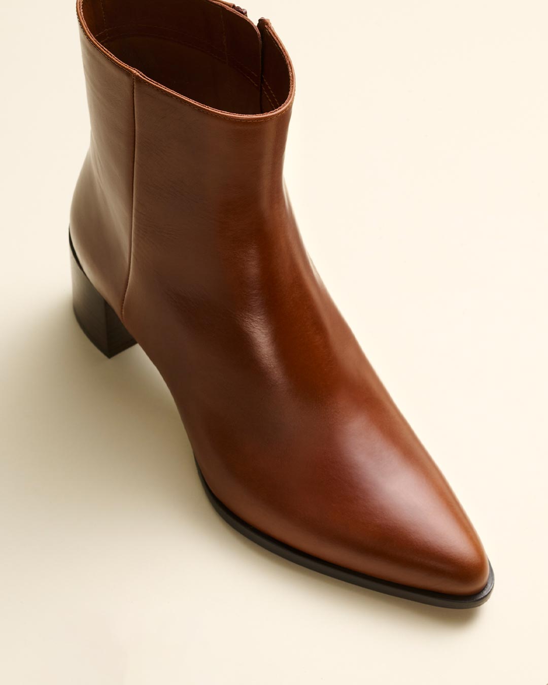 A single brown leather ankle boot with a pointed toe and a mid-height block heel, photographed on a light beige background.