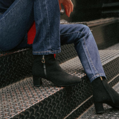 The Bowery Boot in Black Suede, crafted from luxurious Italian suede featuring a sleek almond toe, elegant breasted heel, and a gold-tone buckle detail. 