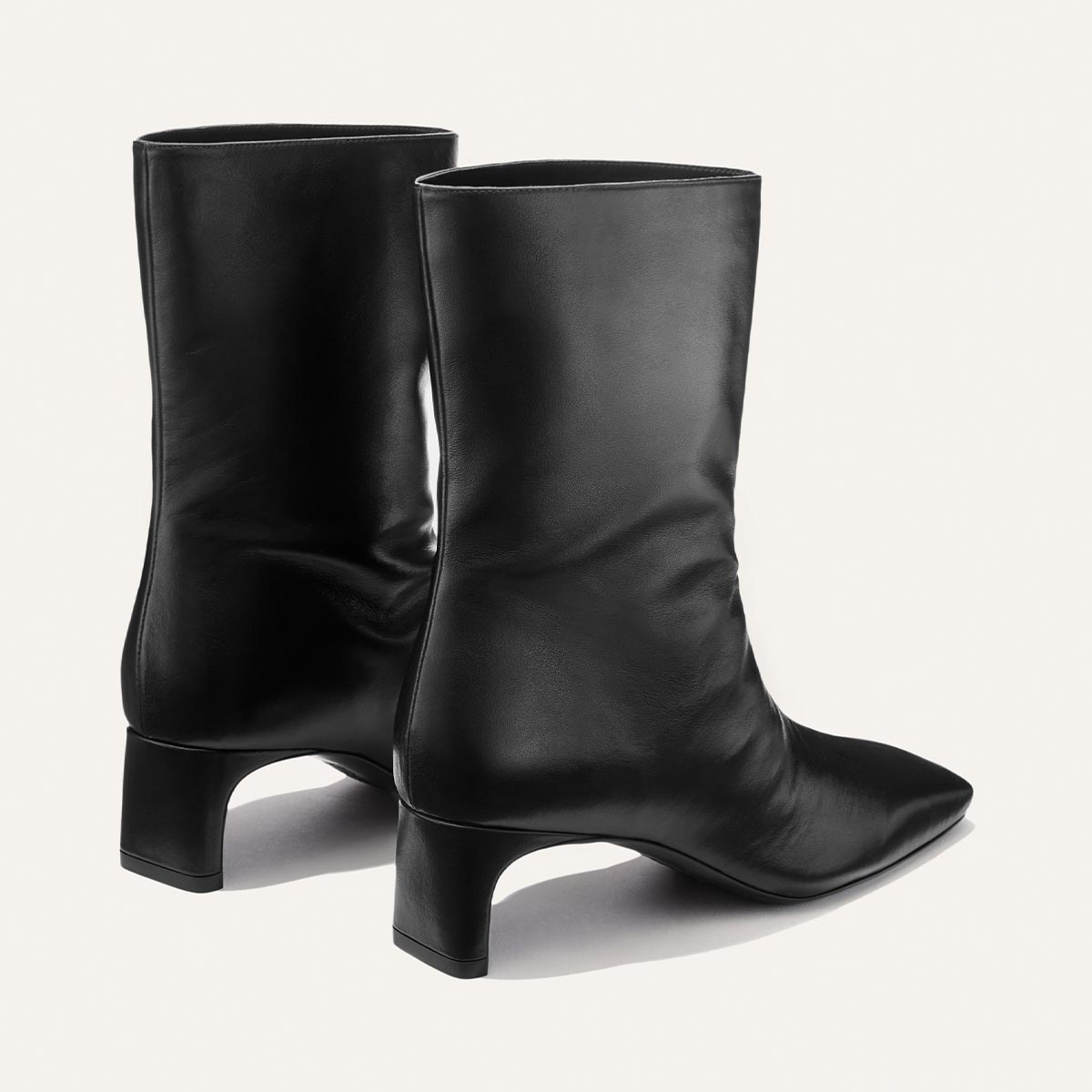 A pair of black, mid-calf leather boots—The Brera Boot in Black Nappa by Margaux—with low, flared heels and pointed toes, displayed against a plain light background.
