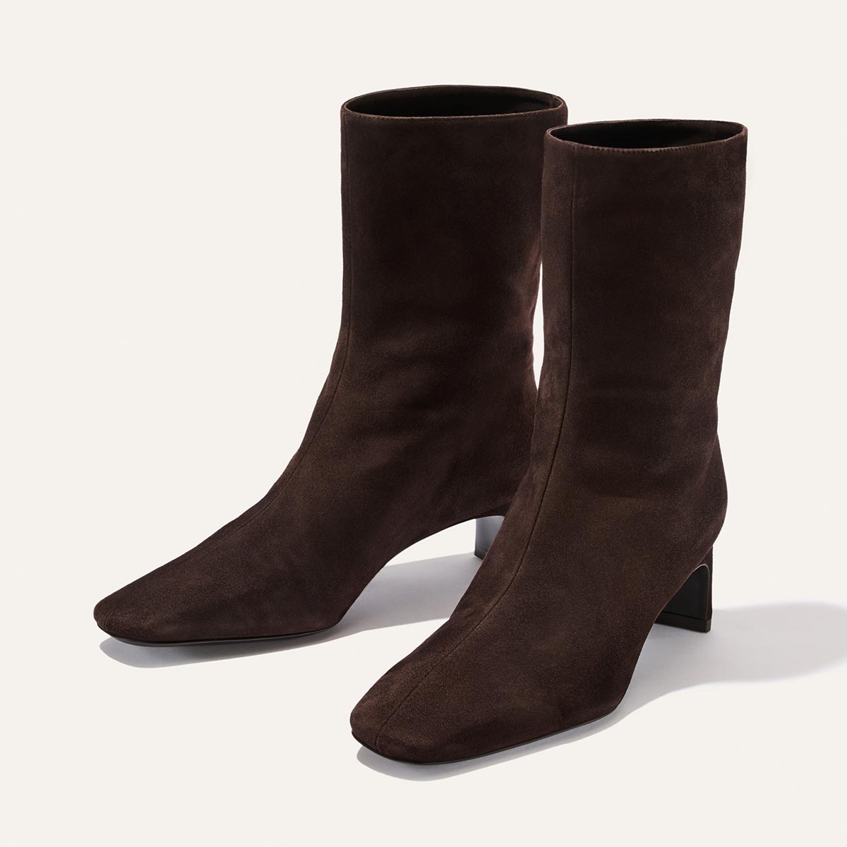 A pair of Margaux’s The Brera Boot in Molasses Suede, featuring a dark brown suede finish, square toe, and low angled block heels, shown against a light background.