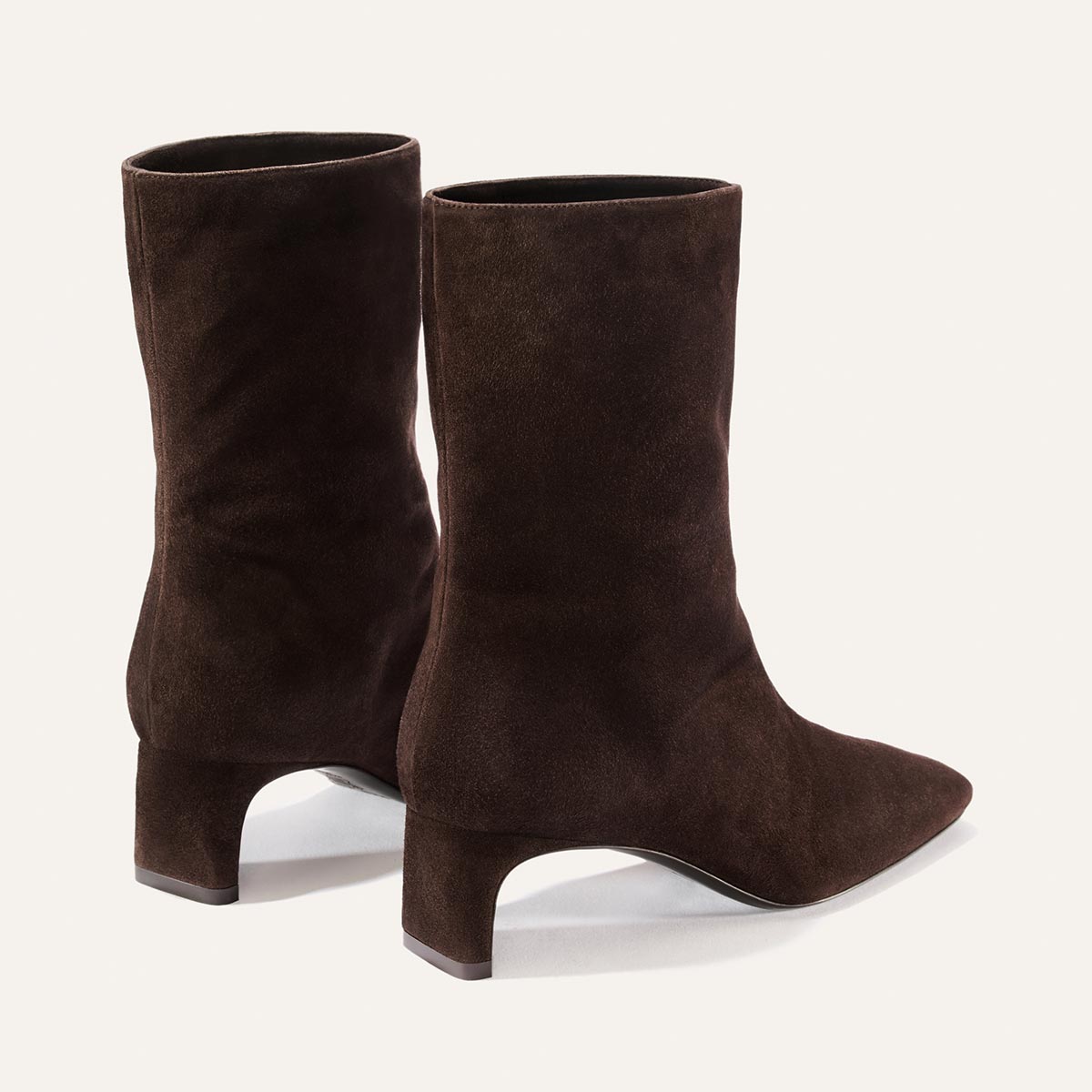 The Brera Boot - Molasses Suede by Margaux, a pair of brown suede mid-calf boots featuring a pointed toe and curved block heel, is displayed on a light background.