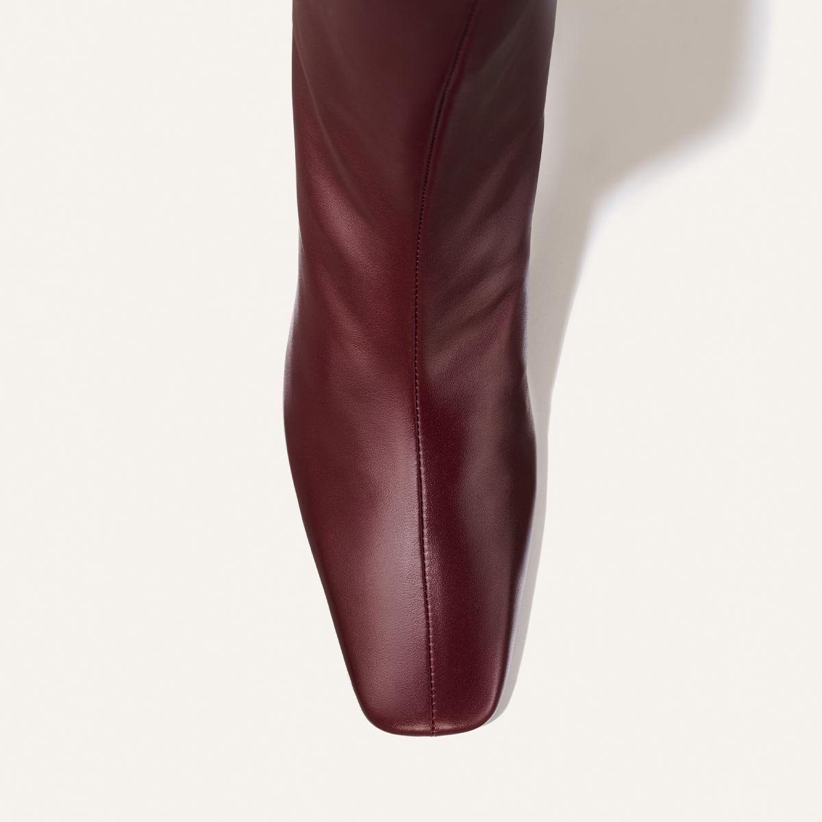 A close-up of The Brera Boot - Merlot Calf, a deep red, square-toe leather knee-high boot featuring a center seam and a 2″ heel.
