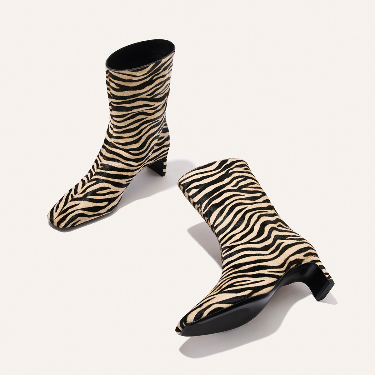 The Brera Boot - Tan Zebra Haircalf is a pair of square toe, mid-calf boots with a tan and black zebra print pattern and a 2″ block heel.