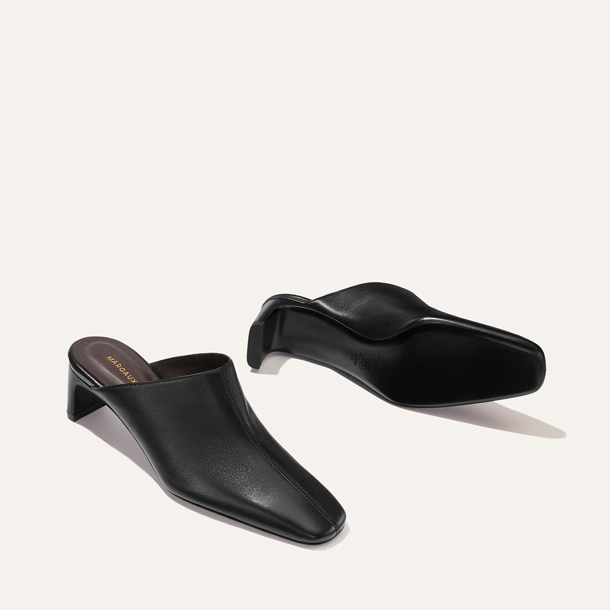 The Brera Mule - Black Nappa by Margaux: a pair of black heeled mules featuring a square toe and low block heel, shown on a plain light background—one shoe upright, the other lying on its side.