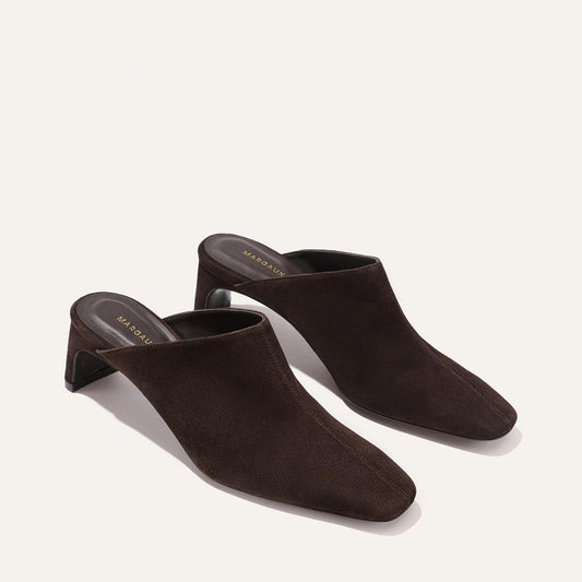 The Brera Mule - Molasses Suede by Margaux, a pair of dark brown suede mules with square toes, a high vamp, and mid-height block heels for an elegant silhouette, displayed on a light background.