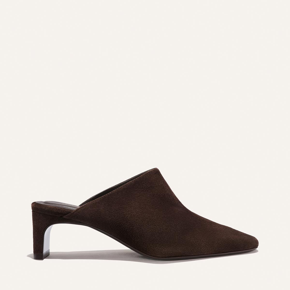 The Brera Mule in Molasses Suede by Margaux features a pointed toe, high vamp, and mid-height sculpted heel, showcased in side profile against a plain off-white background.