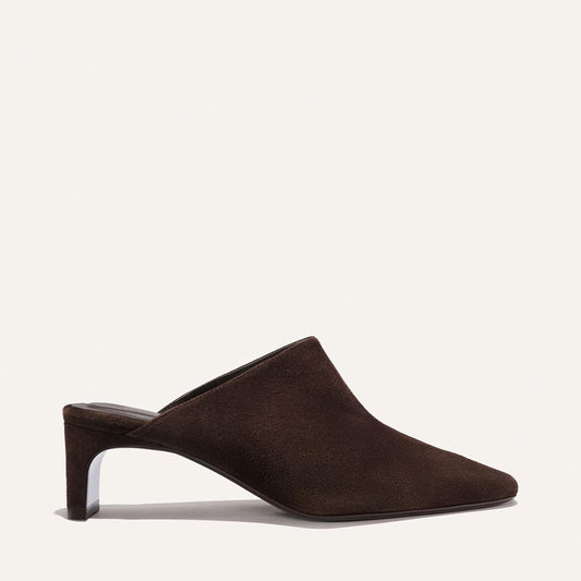 The Brera Mule in Molasses Suede by Margaux features a pointed toe, high vamp, and mid-height sculpted heel, showcased in side profile against a plain off-white background.