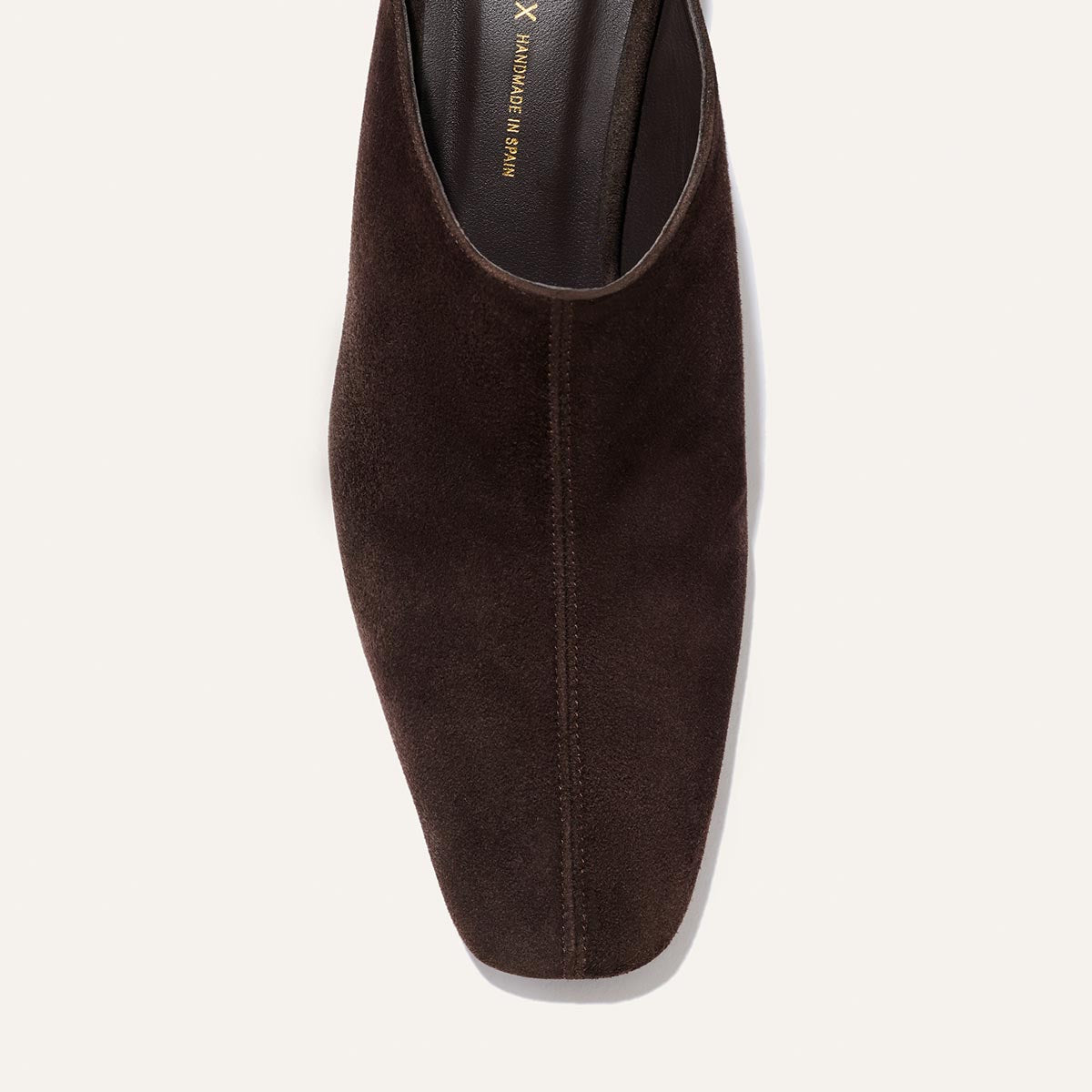 Overhead view of The Brera Mule in Molasses Suede by Margaux, showcasing a softly squared toe and a distinctive center seam, elegantly silhouetted against a light background.