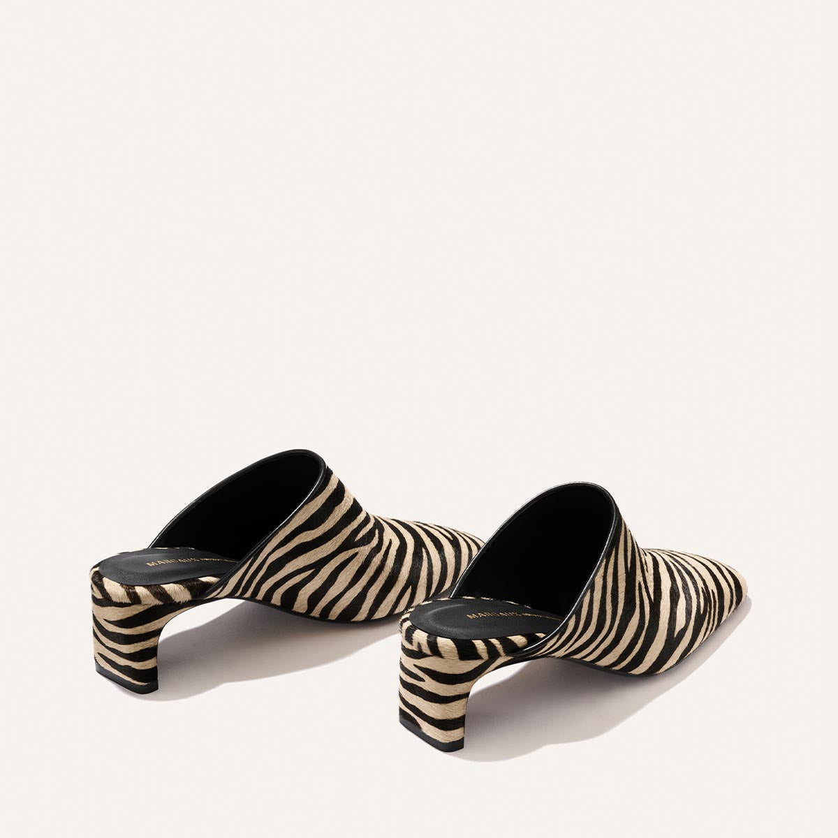 The Brera Mule - Tan Zebra Haircalf by Margaux features a stylish slip-on design with black and beige zebra stripes, short block heels, and black interior soles, set against a simple light background.