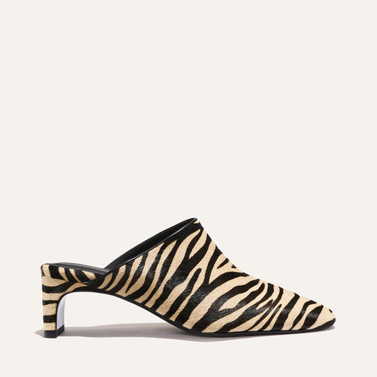 The Brera Mule - Tan Zebra Haircalf by Margaux is a heeled mule with a pointed toe, showcasing a black and beige zebra print pattern, photographed against a plain light background.