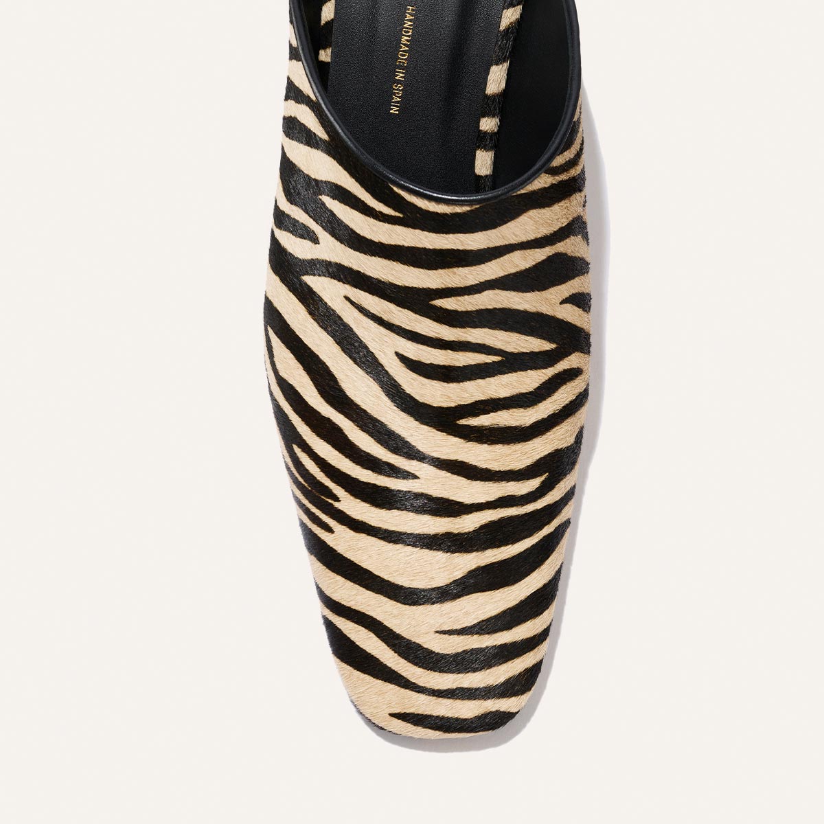 A close-up of the Margaux Brera Mule in Tan Zebra Haircalf, viewed from above, highlights its pointed toe and part of the opening, showcasing the distinctive black and beige zebra stripe pattern.