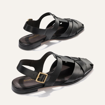 Black sandals with gold buckles on a light gray background
