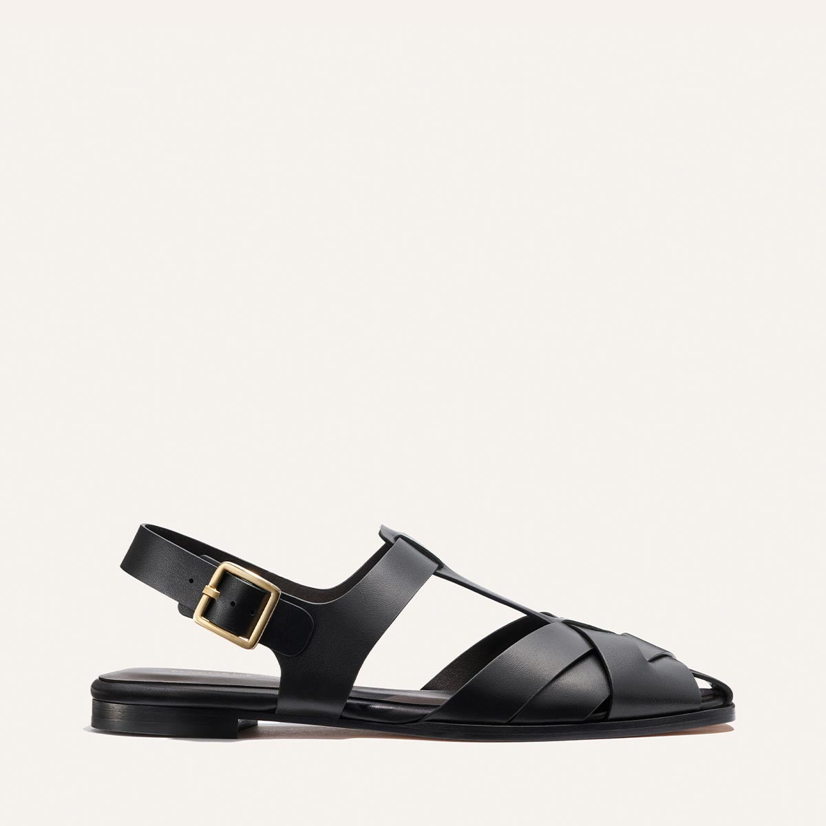 Black sandal with a gold buckle on a light gray background