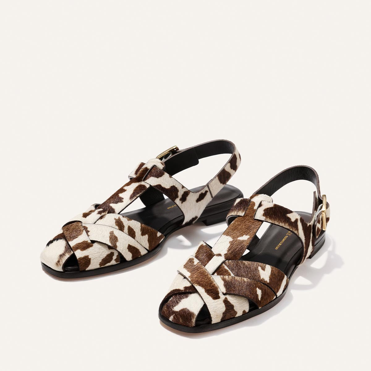 Pair of sandals with a cow print pattern on a light beige background