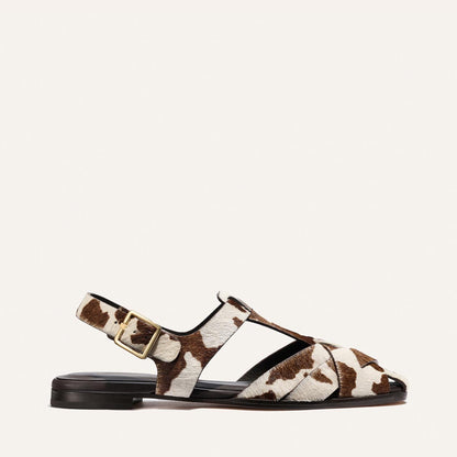 Brown and white cow print sandal with a gold buckle on a light beige background
