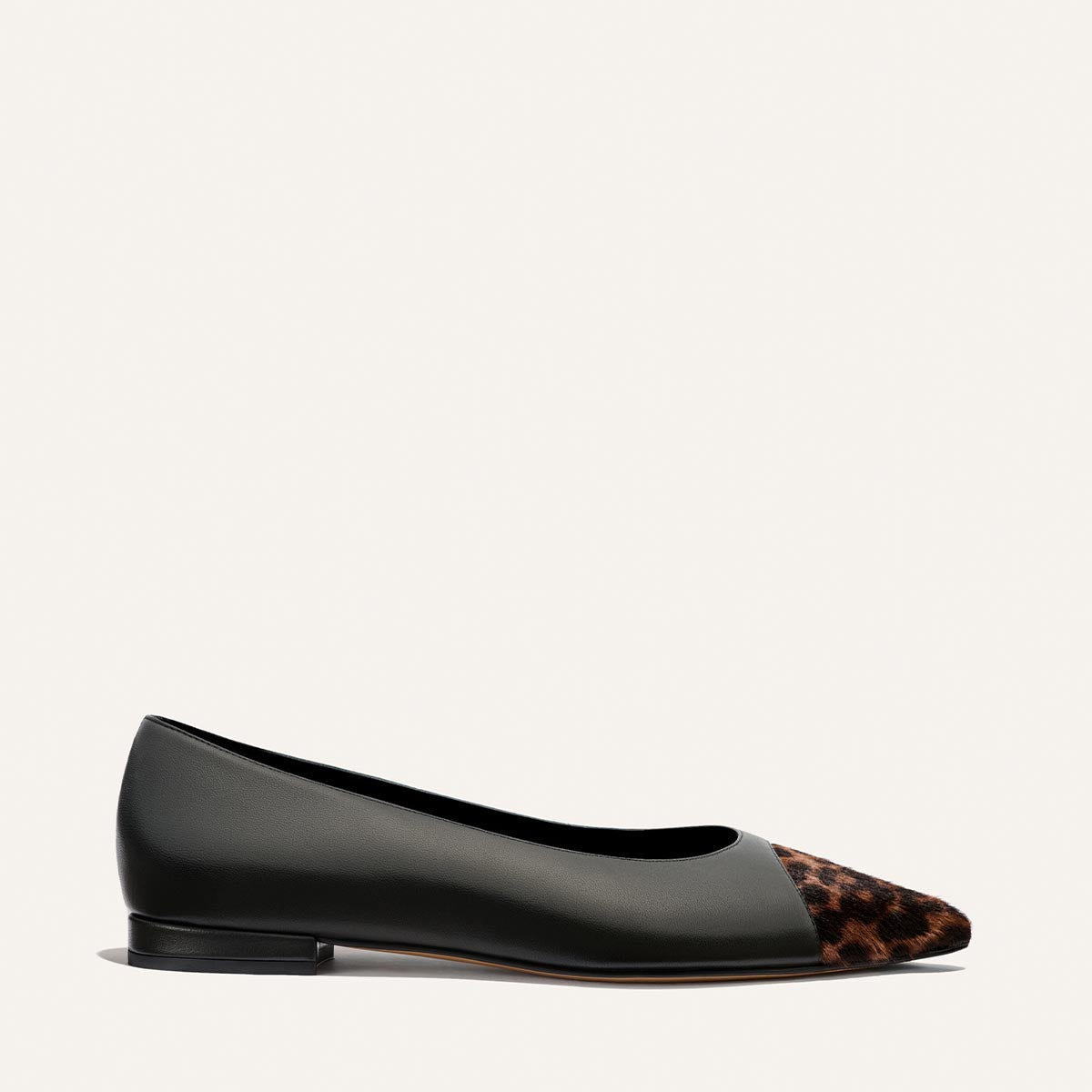 The Alba by Margaux is a black nappa leather ballet flat with a pointed toe, featuring brown and black leopard haircalf detailing. Shown from a side view on a light background, this shoe is designed for comfort and includes a padded insole.