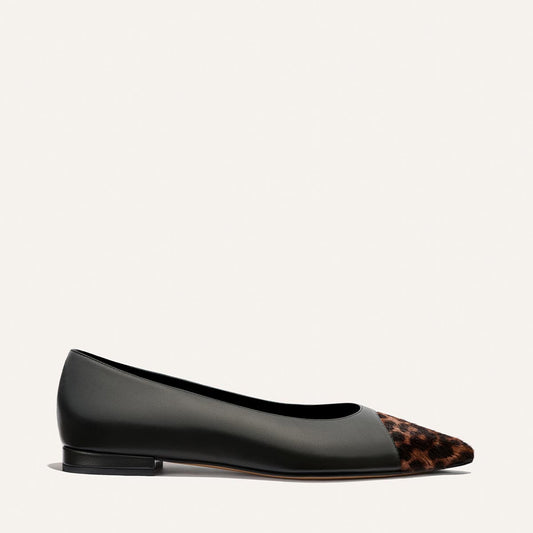 The Alba by Margaux is a black nappa leather ballet flat with a pointed toe, featuring brown and black leopard haircalf detailing. Shown from a side view on a light background, this shoe is designed for comfort and includes a padded insole.