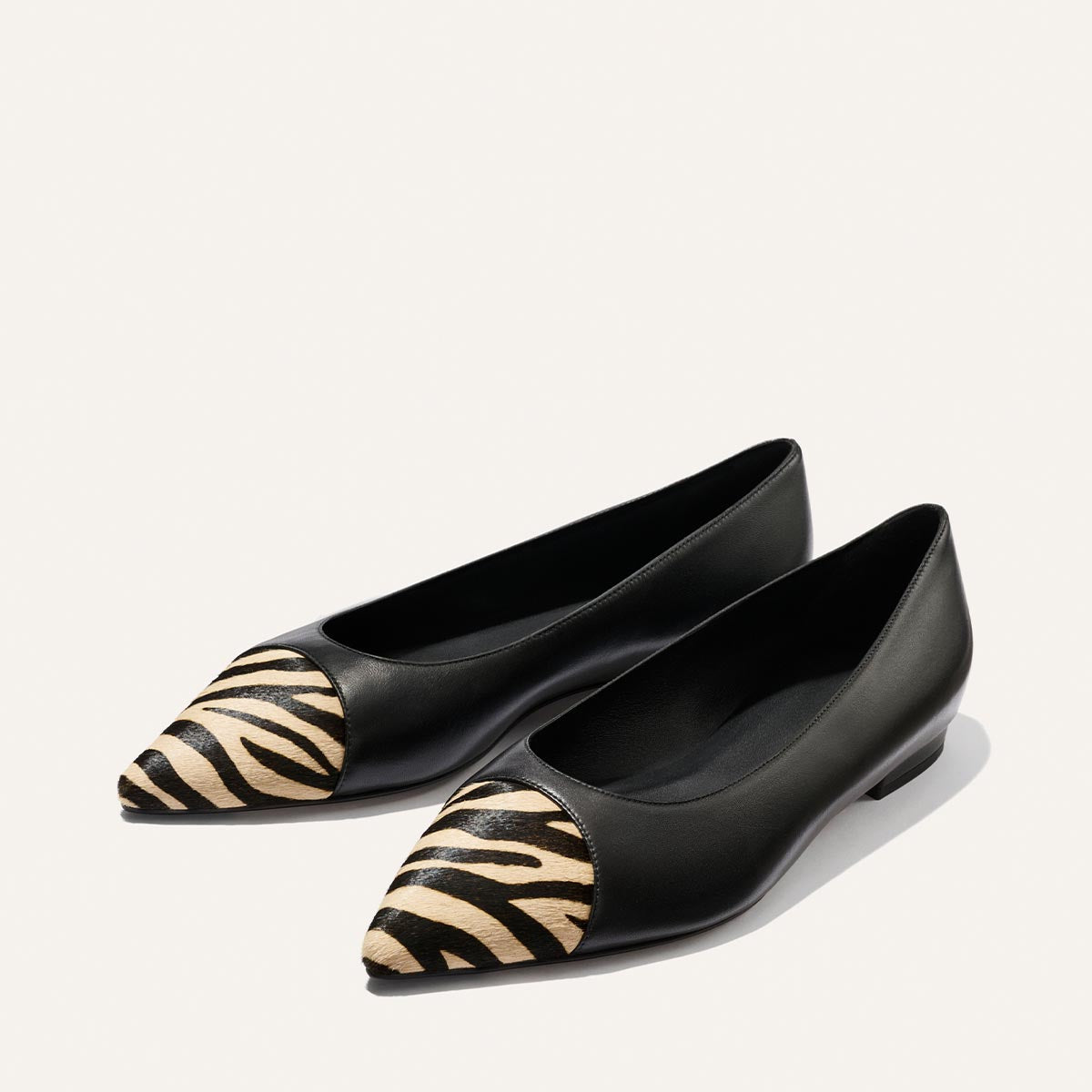 A pair of Margaux’s The Alba flats in Black Nappa and Zebra Haircalf, featuring pointed toes, zebra print detail at the toe, and a comfortable padded insole, displayed side by side on a plain light background.