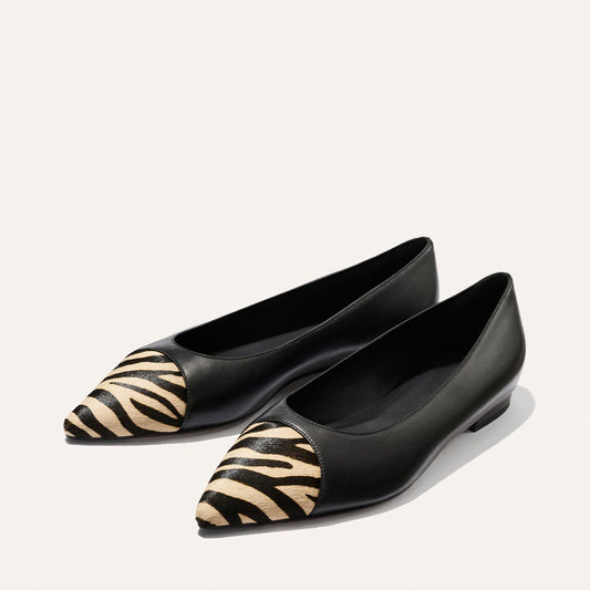 A pair of Margaux’s The Alba flats in Black Nappa and Zebra Haircalf, featuring pointed toes, zebra print detail at the toe, and a comfortable padded insole, displayed side by side on a plain light background.