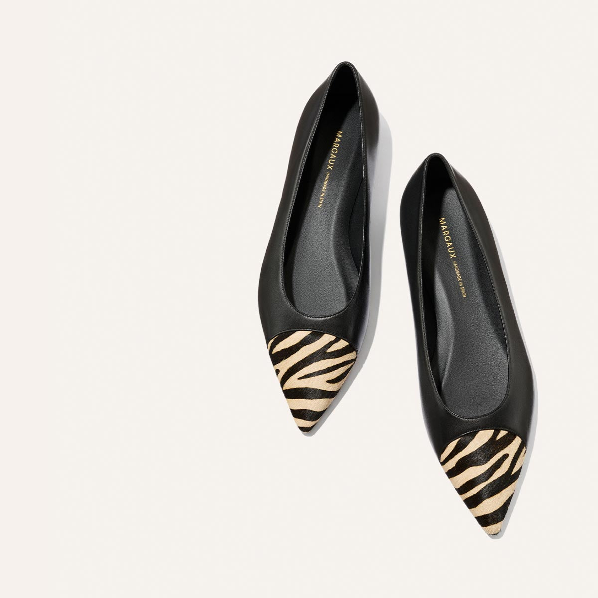 A pair of The Alba flats by Margaux in black nappa with zebra haircalf pointed-toe caps and a comfortable padded insole, displayed on a plain white background.