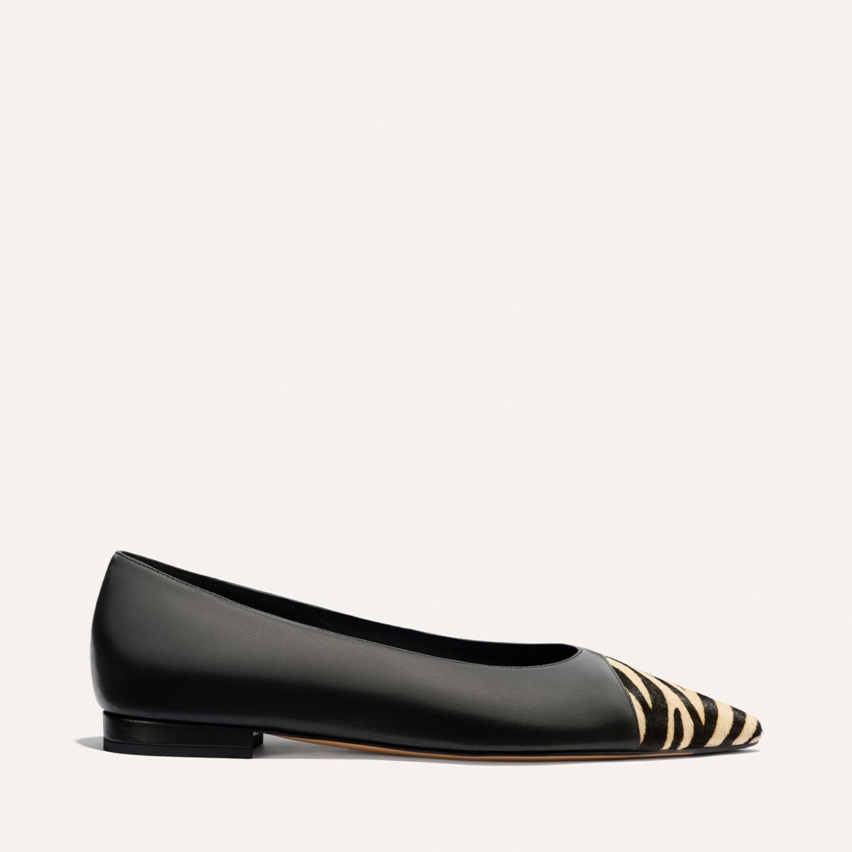 Introducing The Alba by Margaux: a black nappa ballet flat with a pointed toe, featuring a tan and black zebra haircalf pattern on the tip and a cushioned padded insole for added comfort.