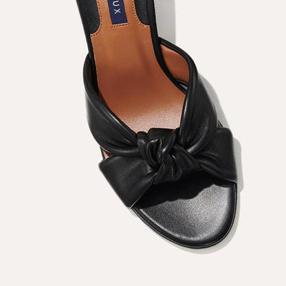 The Carmine Mule in Black Nappa, a slide-on heel featuring a plush knot detail and comfortable 2.5-inch block heel