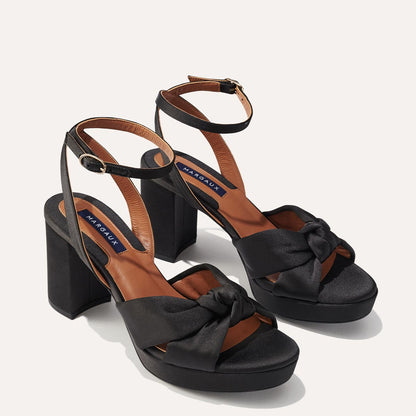 The Carmine Platform in Black Satin featuring a plush knot detail, a comfortable 1-inch platform, and a 3.5-inch block heel.