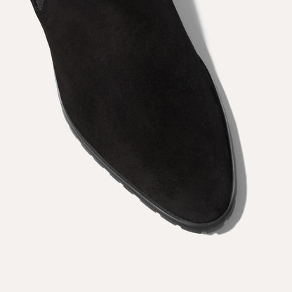 Close-up of Margaux's The Chelsea Boot in black suede, showcasing its rounded toe and visible sole against a light background.