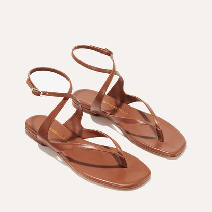 The Palermo Sandal - Saddle Nappa by Margaux features brown leather straps, ankle buckles, flat soles, and a minimalist design—ideal for summer days and shown against a light background.