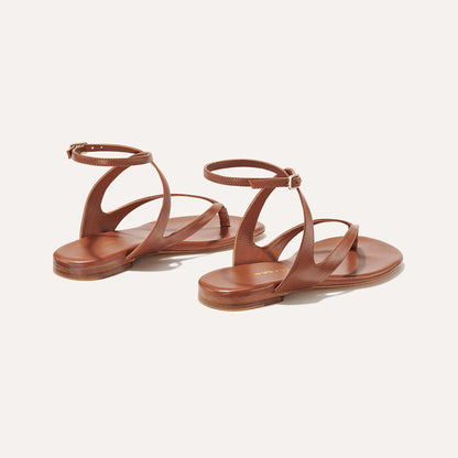 The Palermo Sandal - Saddle Nappa by Margaux: brown leather flat sandals with ankle and curved side straps, plus a cushioned insole—ideal for summer days. Shown against a plain off-white background.