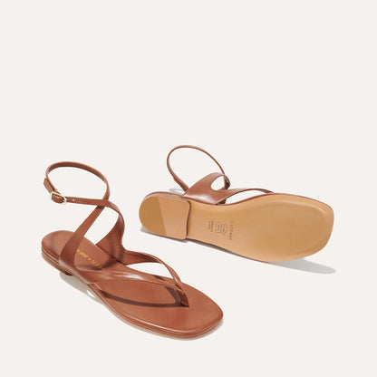 The Palermo Sandal - Saddle Nappa by Margaux: brown strappy flat sandals with ankle straps, buckle closures, and cushioned insoles. One sandal stands upright, the other shows the sole against an off-white background.