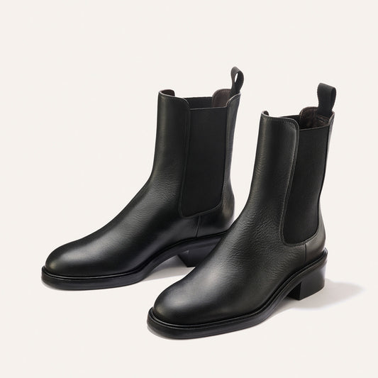 A pair of Margaux’s The City Chelsea Boot in black calf leather, featuring elastic side panels and low heels, displayed on a light background.