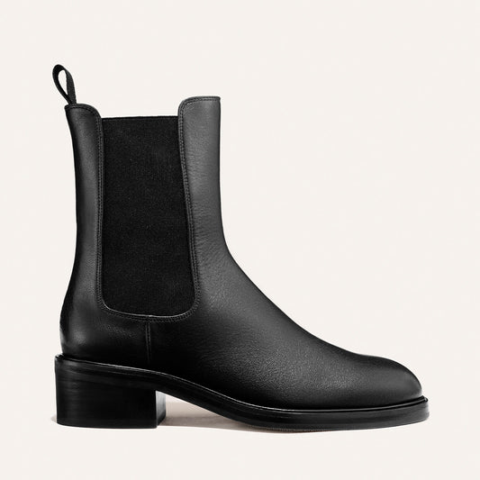 Introducing The City Chelsea Boot - Black Calf by Margaux: a sleek black leather Chelsea boot featuring a round toe, elastic side panels, and a convenient pull tab at the back. This boot is designed with a low, chunky heel and showcases a smooth, polished finish.