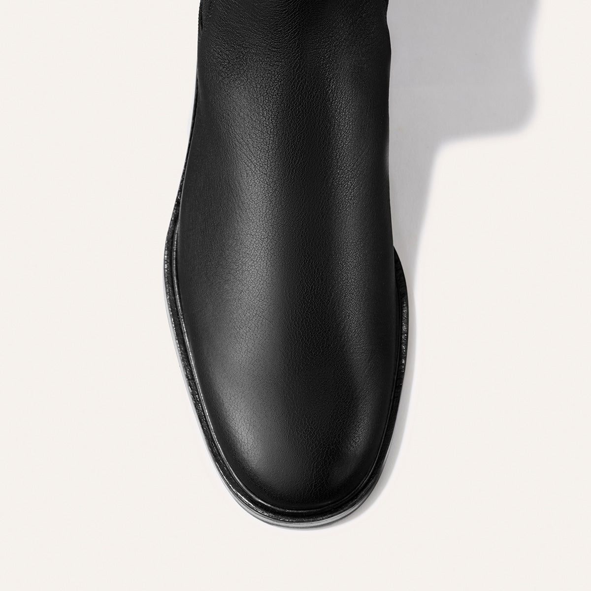 Top view of Margaux’s The City Chelsea Boot in Black Calf, featuring smooth black leather with a rounded toe, displayed against an off-white background.